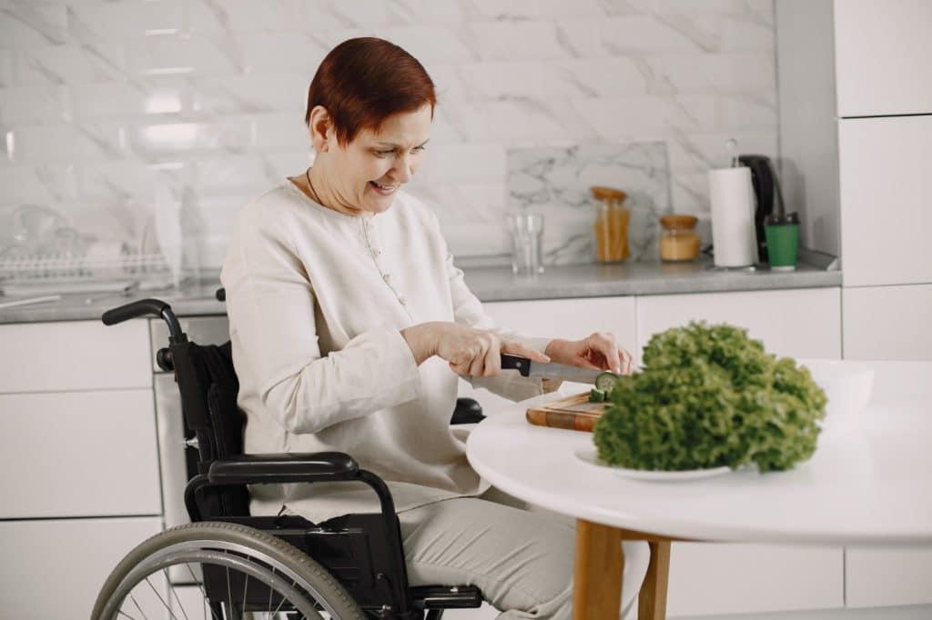 A person in a wheelchair cutting vegetables Description automatically generated